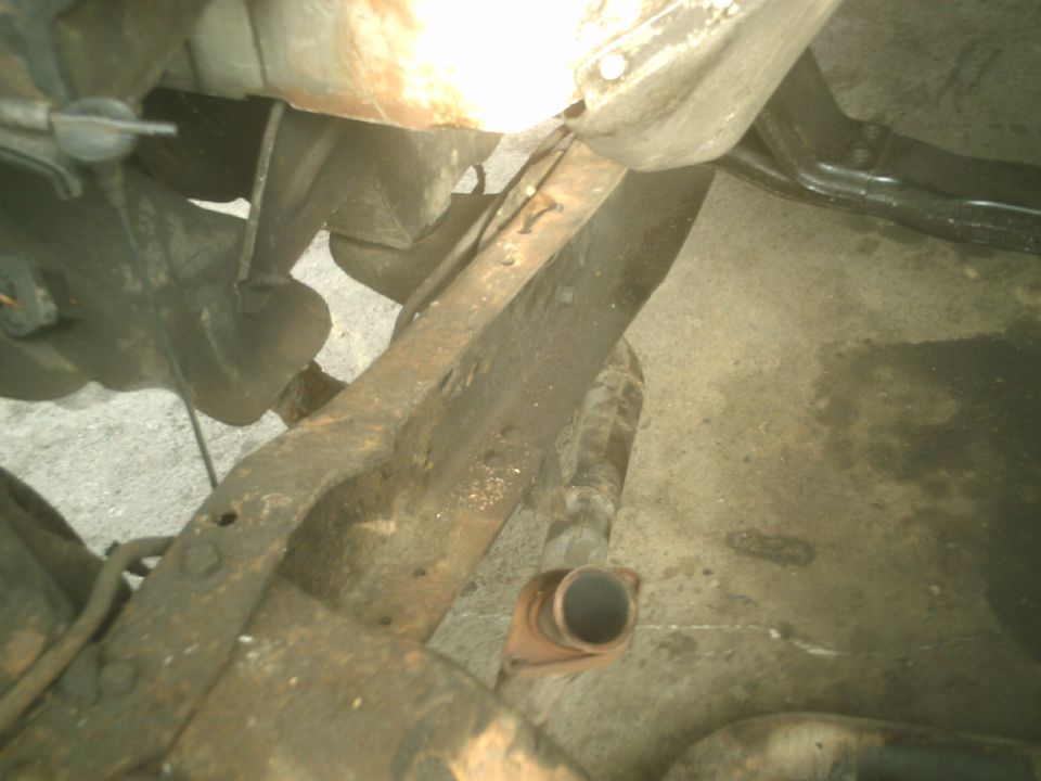 Close-up of rusty vehicle undercarriage with frame and exhaust pipe.