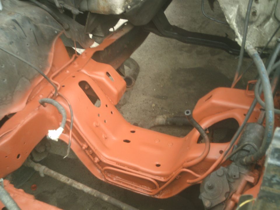 Overhead view of an orange painted vehicle subframe with hoses and mechanical parts.