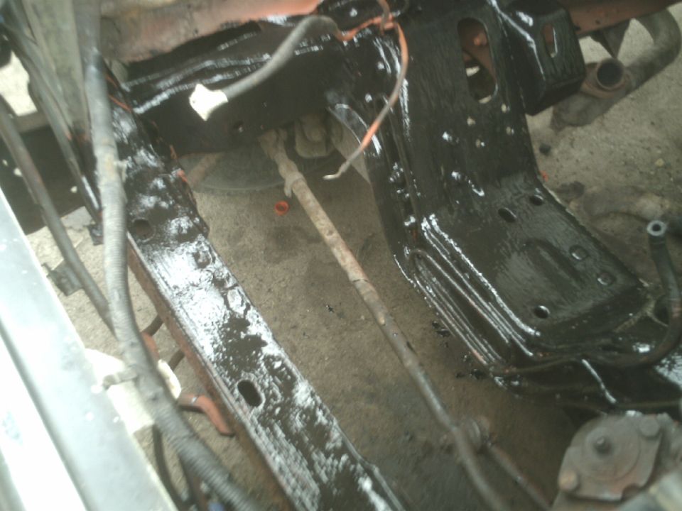 Underside of a vehicle frame with black paint and rust.