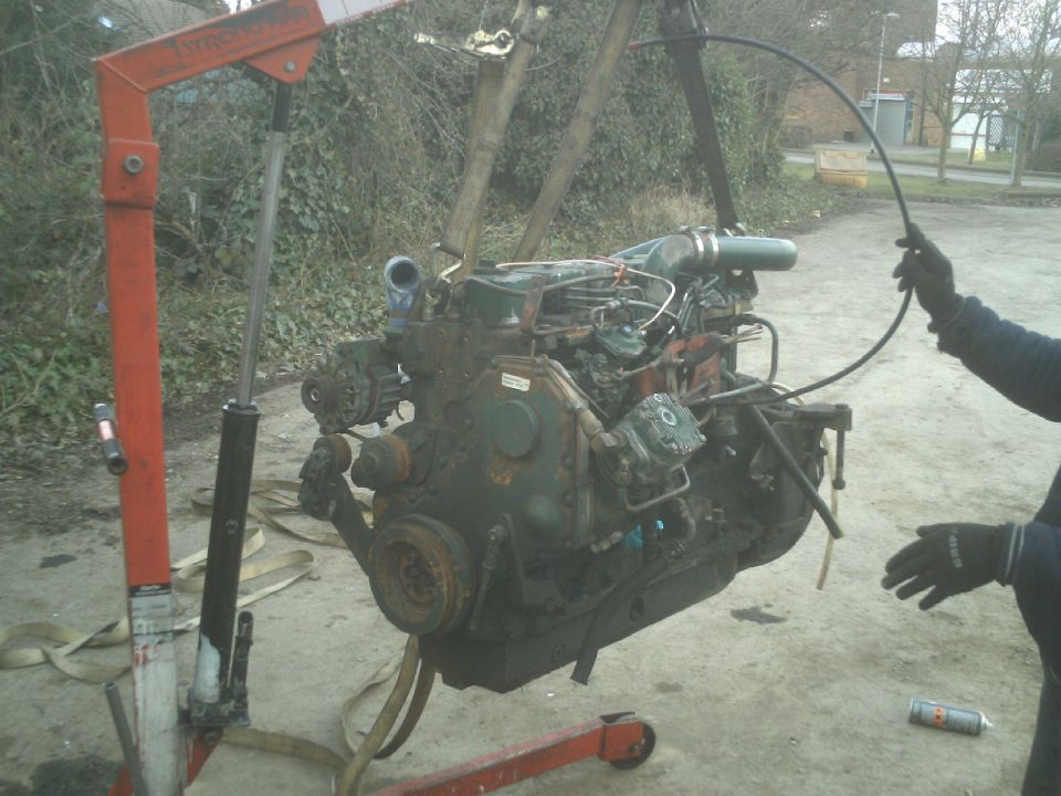 Green engine suspended by red engine hoist, person holding hose.