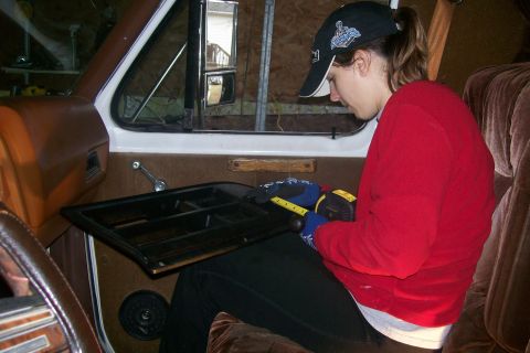 1982 Ford E350 - A person wearing a red sweatshirt and a baseball cap is sitting inside a vehicle, holding a tape measure to a black dashboard component. Th…