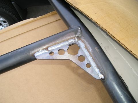 1986 Toyota Hilux - A close-up view of a welded metal bracket with circular cutouts attached to a black metal tube, likely part of a roll cage or frame modific…