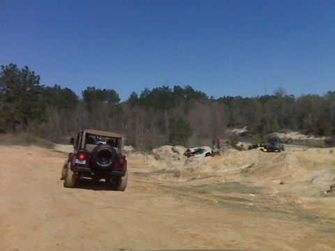 2008 Jeep Wrangler - A tan soft-top Jeep Wrangler is driving on a dirt road in a sandy, off-road park. Several other off-road vehicles are visible in the backgr…
