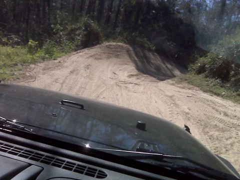 2008 Jeep Wrangler - The front view of a dark colored Jeep Wrangler driving up a sandy hill with trees in the background. The hood and windshield wipers are vis…