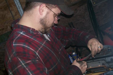 1982 Ford E350 - A person wearing a red plaid shirt and a baseball cap is working on something with dirty hands. The person is wearing glasses and has a bea…