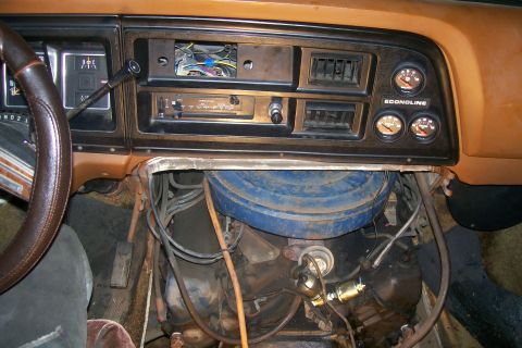 1982 Ford E350 - The interior of a vintage van shows the dashboard with a steering wheel, radio, air vents, and gauges. The engine is visible below the dash…