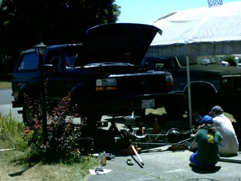 1995 Ford Bronco - A black Ford Bronco is being worked on, with its hood up and the vehicle elevated on jack stands.