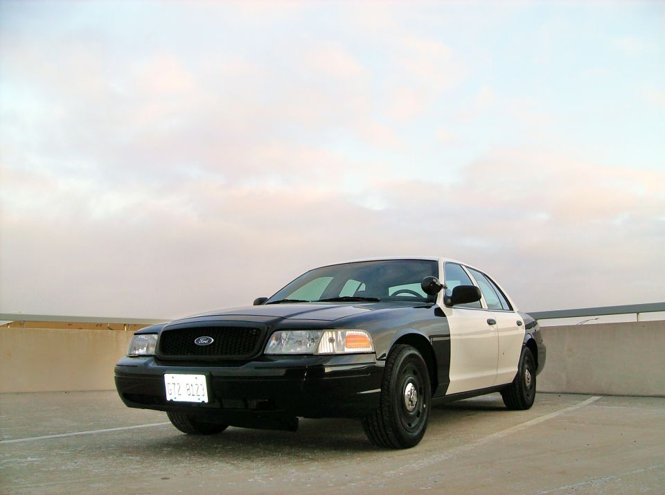 Black and white Ford Crown Victoria police car parked outdoors under a cloudy sky