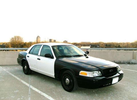 2004 Ford Crown Victoria - A two-tone sedan, with a black front and white rear, is parked in an outdoor lot with a city skyline visible.