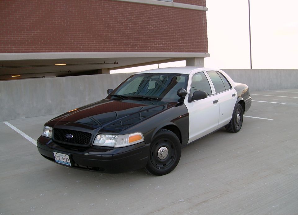 Black and white police car parked on a concrete level of a parking garage. License plate is visible
