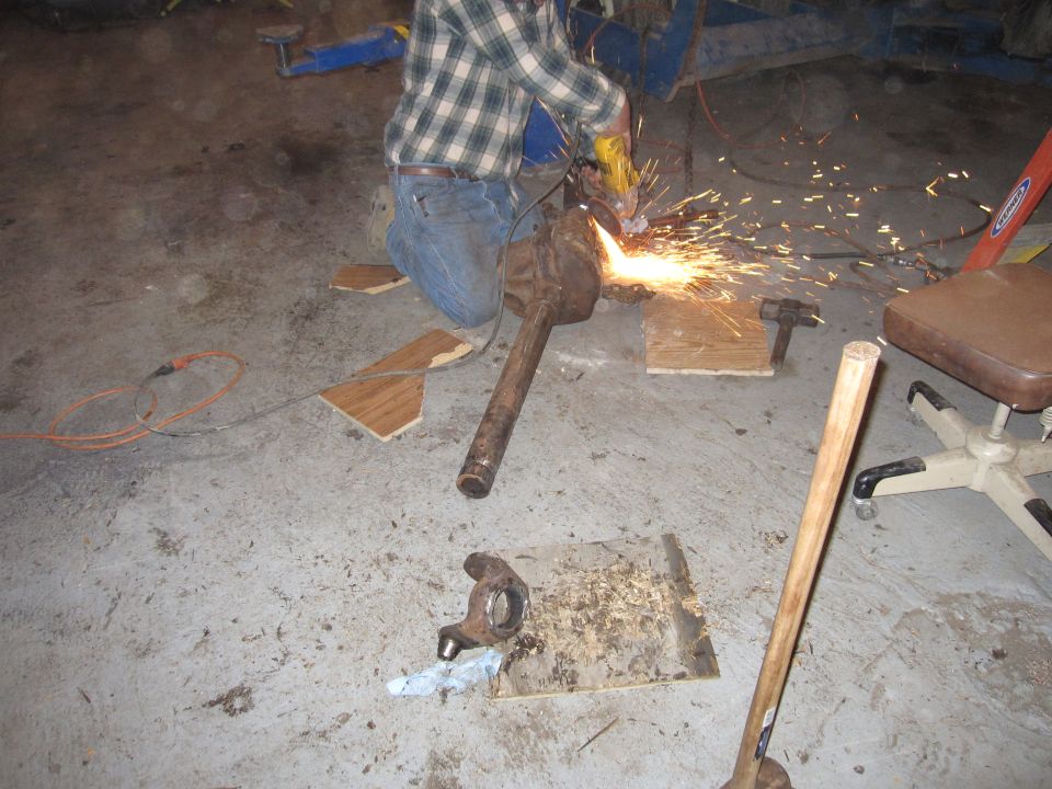 guy in plaid shirt and jeans grinding metal with sparks flying, parts on floor