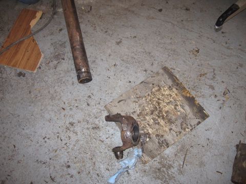 1992 Ford Bronco - A rusty metal part, possibly a spindle or knuckle, lies on a concrete floor next to a metal shaft.