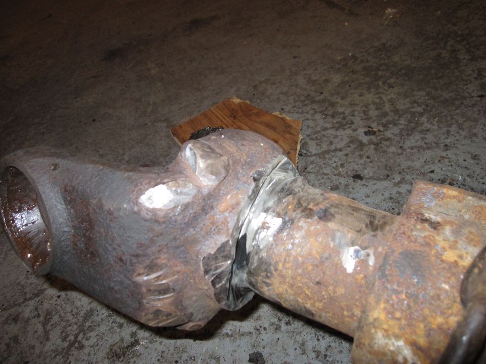rusted metal pipe section with visible welds and a piece of wood underneath