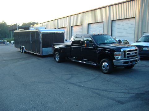 2002 Ford F-150 - A black Ford Super Duty truck is parked outside a building, hitched to a large black cargo trailer.