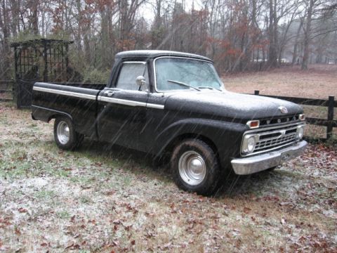 1966 Ford F-100 - A black Ford F-series pickup truck sits in a snowy yard, its chrome grille and trim visible.