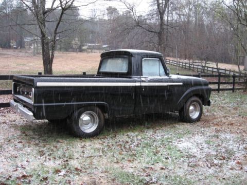 1966 Ford F-100 - A black 1966 Ford F-100 pickup truck sits in a field during a light snowfall.