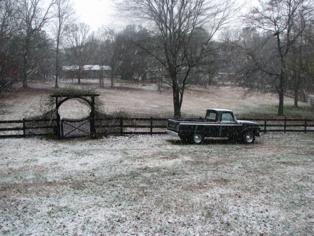 1966 Ford F-100 pickup truck parked in a snowy field next to a wooden fence and gate