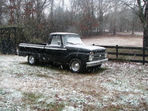 1966 Ford F-100 - A classic black pickup truck sits in a field as snow falls around it.