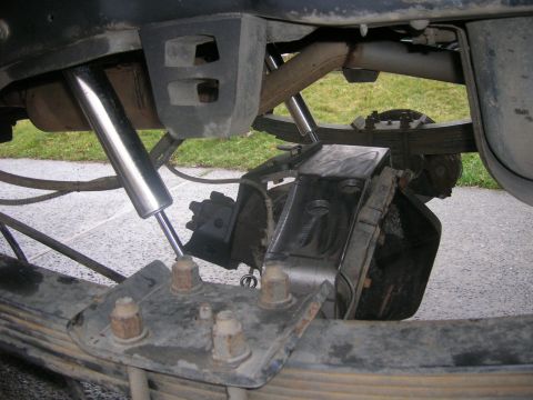 1996 Ford Bronco - Under-vehicle view of a rear leaf-spring suspension with U-bolts through a spring plate, a chrome-bodied shock, and the axle housing with a…