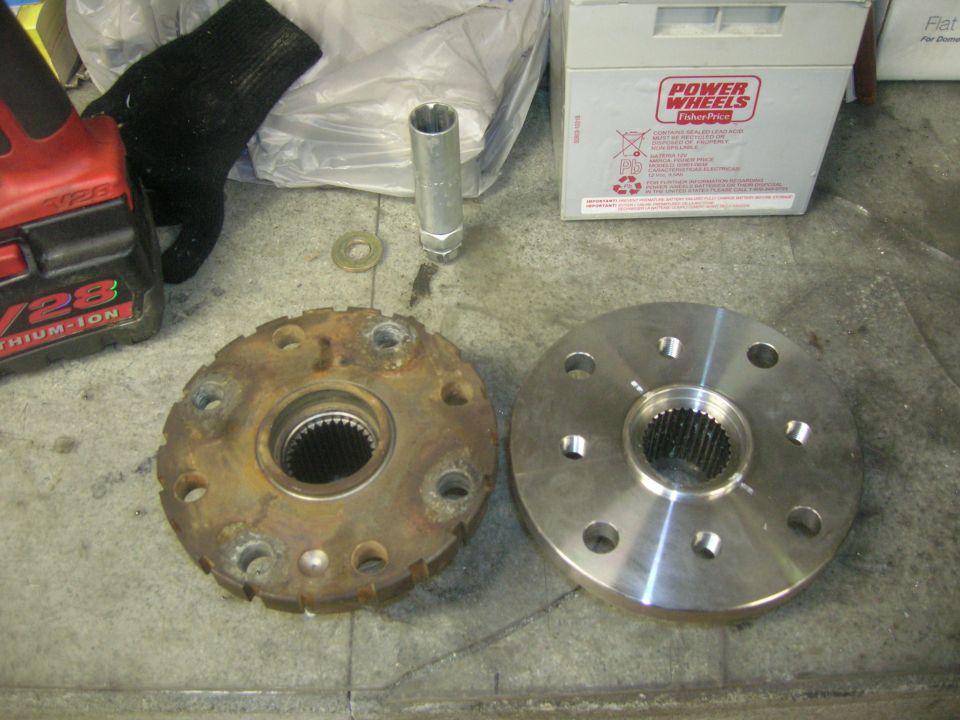 Rusty old wheel hub next to a shiny new one on a concrete floor. Power Wheels battery box in background