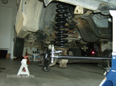 1990 Ford Bronco - The vehicle is on jack stands, showing the underside of the suspension system and steering components.