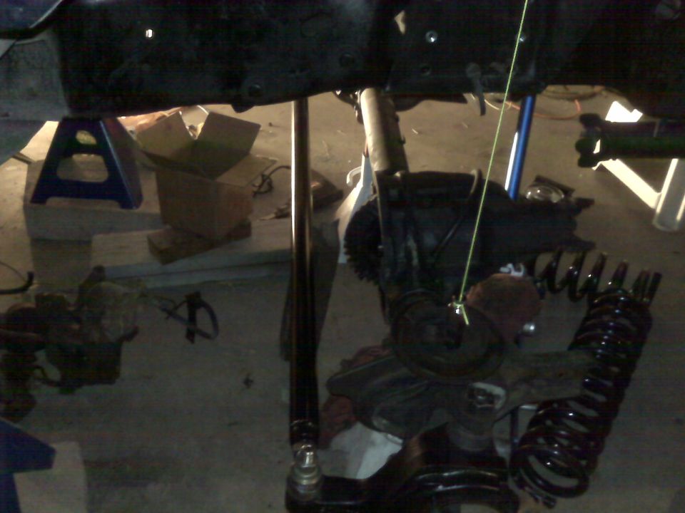 Vehicle suspension parts, including a differential and coil spring, are visible under a dark chassis