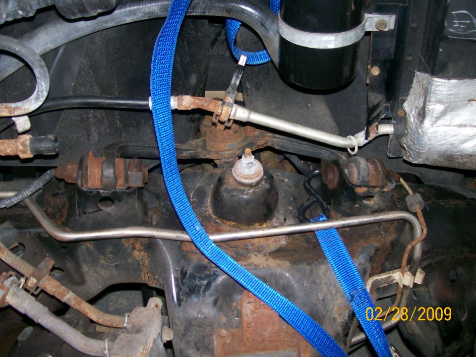 Close-up of rusty vehicle suspension parts and blue tie-down straps. Date stamp reads 02/28/2009