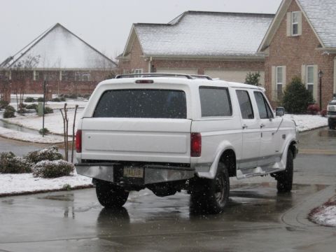 1978 Ford Bronco - A white SUV is parked on a wet driveway as snow falls around it.