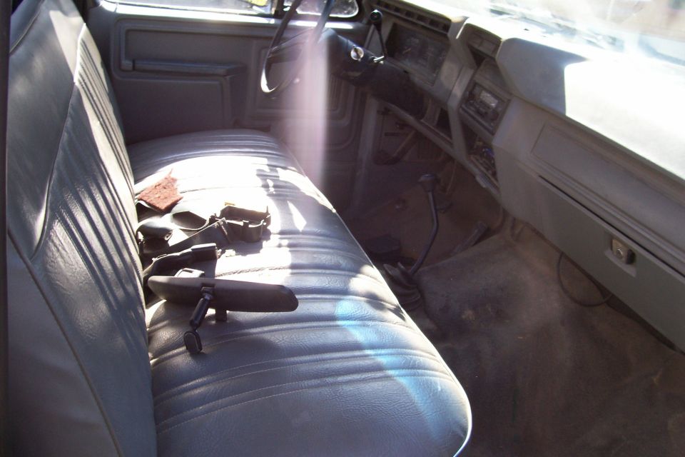 Gray vinyl bench seat in a truck interior, showing a rearview mirror and seatbelts
