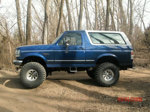 1996 Ford Bronco - Side view of a lifted blue 1996 Ford Bronco with a white top, parked outdoors.