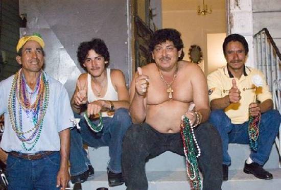 Four men sit on steps wearing Mardi Gras beads. One gives a thumbs up