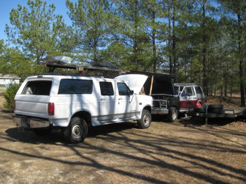 1986 Ford C-350 (Centurion Conversions) - A white extended cab pickup truck with a camper shell is parked next to another vehicle with its hood open.