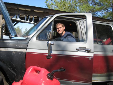 1986 Ford C-350 (Centurion Conversions) - A man sits in the cab of a pickup truck, with the hood open and gas cans nearby.