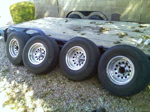 1996 Ford Bronco - Four aftermarket wheels and tires are loaded onto a flatbed trailer.