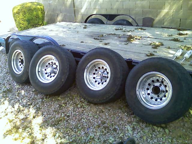 four aftermarket wheels with tires on a flatbed trailer