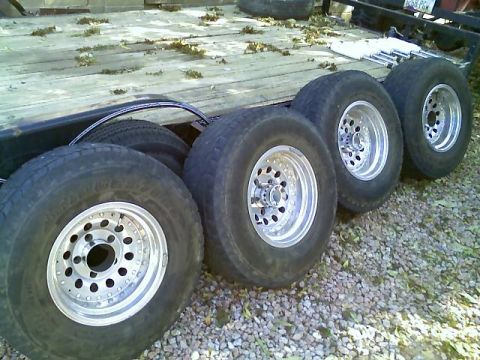 1996 Ford Bronco - Several tires and their aluminum alloy rims are loaded onto a trailer, resting on a gravel surface.