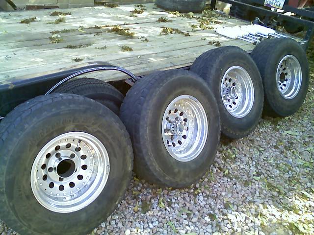 four tires with shiny rims sitting on a wooden trailer bed