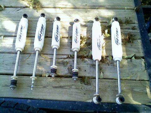1996 Ford Bronco - Six Pro Comp shock absorbers are displayed on a wooden surface, with visible text on each part.