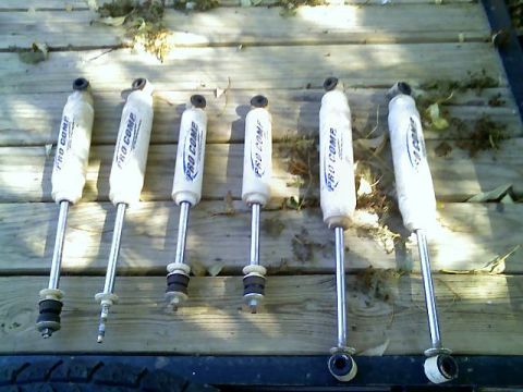 1996 Ford Bronco - Several Pro Comp shock absorbers are displayed on a wooden surface, with some leaves scattered around.