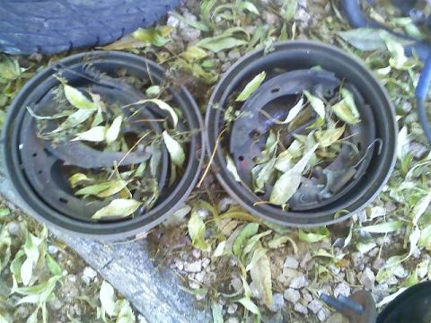 1996 Ford Bronco - Two brake drums filled with leaves sit on the ground next to a tire.