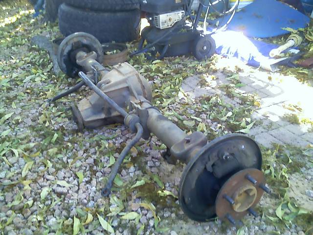 Rear axle assembly with brake drum and hub, lying on gravel and leaves
