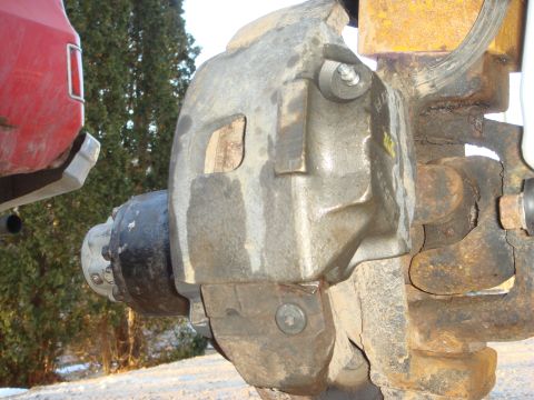 1978 Chevrolet C/K Pickup - Close-up of a heavy-duty brake caliper and hub assembly, partially obscuring a red vehicle fender.