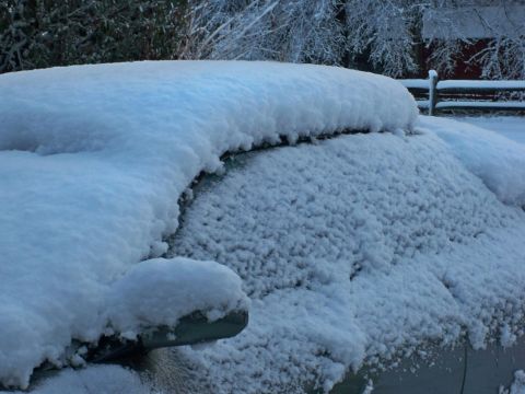 1995 Ford Probe - A car is heavily covered in snow, obscuring its details, with a rural winter scene behind it.
