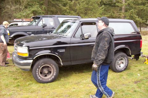 1995 Ford Bronco - Two black Ford Broncos are parked on a grassy area with trees in the background.