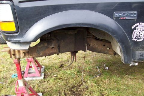 1995 Ford Bronco - The side of a 1995 Ford Bronco XLT is shown on jack stands, revealing its front fender and suspension system.