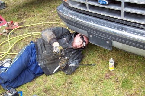 1995 Ford Bronco - Mechanic works on the front end of a 1995 Ford Bronco, with tools and a spray can on the grass.