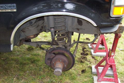 1995 Ford Bronco - The front suspension and wheel of a black 1995 Ford Bronco are visible, supported by red jack stands.