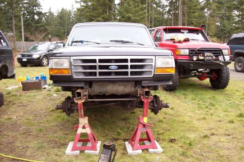 1995 Ford Bronco - Front view of a 1995 Ford Bronco on jack stands, with a red off-road vehicle in the background.