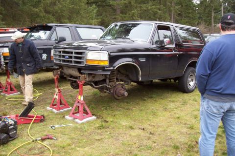 1995 Ford Bronco - A 1995 Ford Bronco is undergoing front-end work, supported by jack stands, with another Bronco visible in the background.