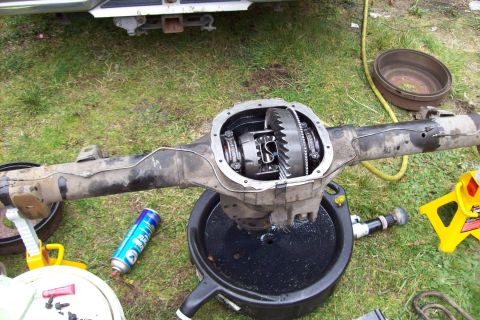 1995 Ford Bronco - A vehicle's differential assembly is shown removed from the vehicle, resting in a drain pan on the grass.